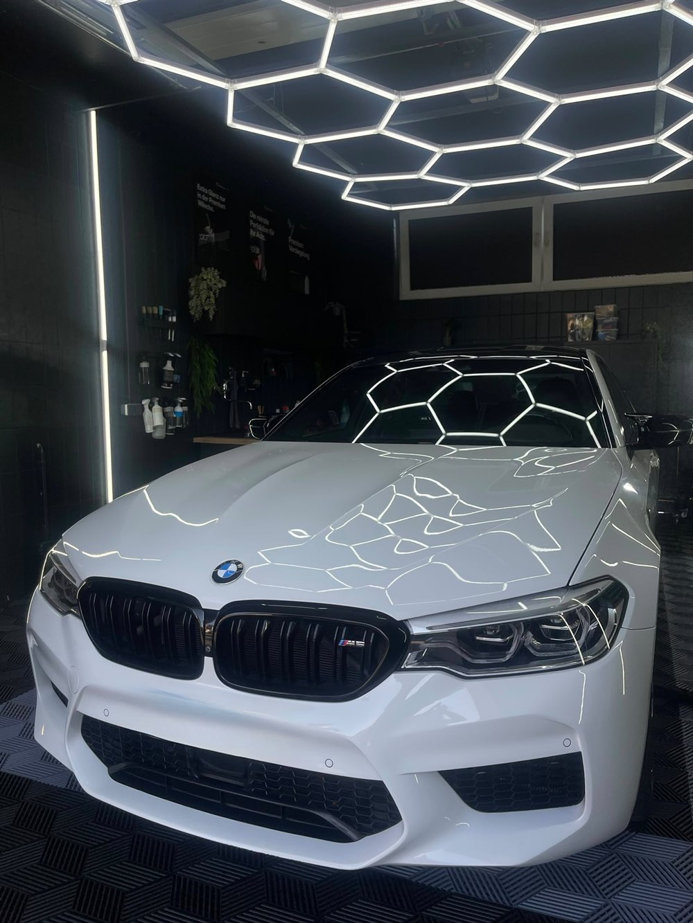Weißer BMW M5 Competition, Frontansicht unter dem Hexagon-Licht im Detailing-Studio in Peine
